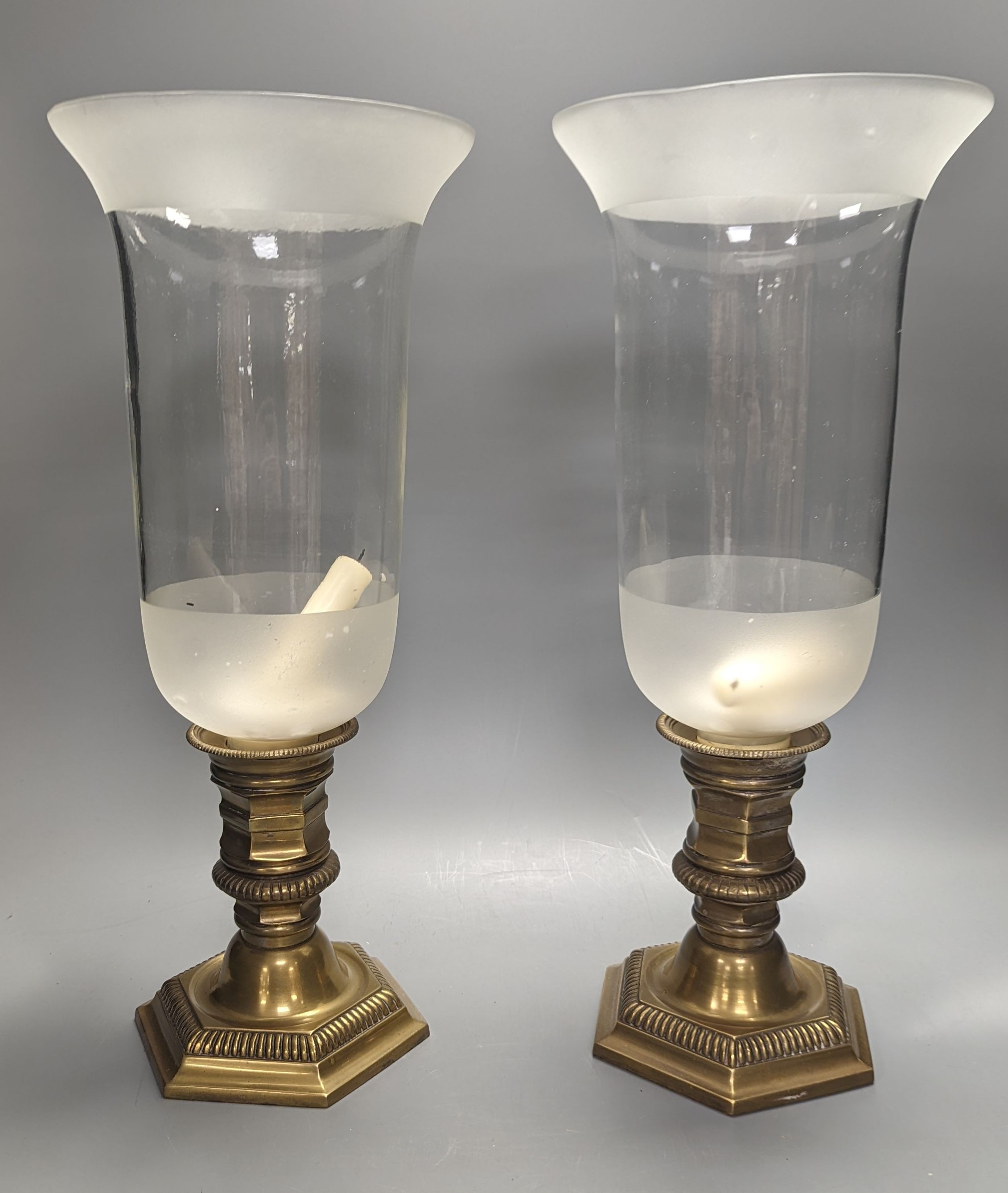 A pair of brass lamps with part frosted glass storm shades, height 45cm